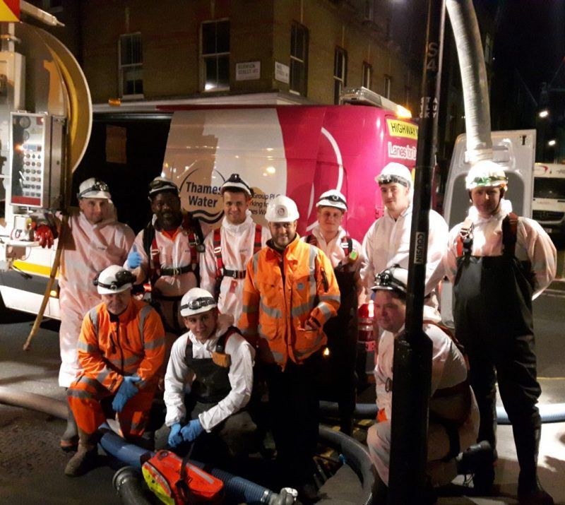 Ten engineers wearing white waterproof overalls and hard hats, standing in front of a Lanes Group PLC van with the words 